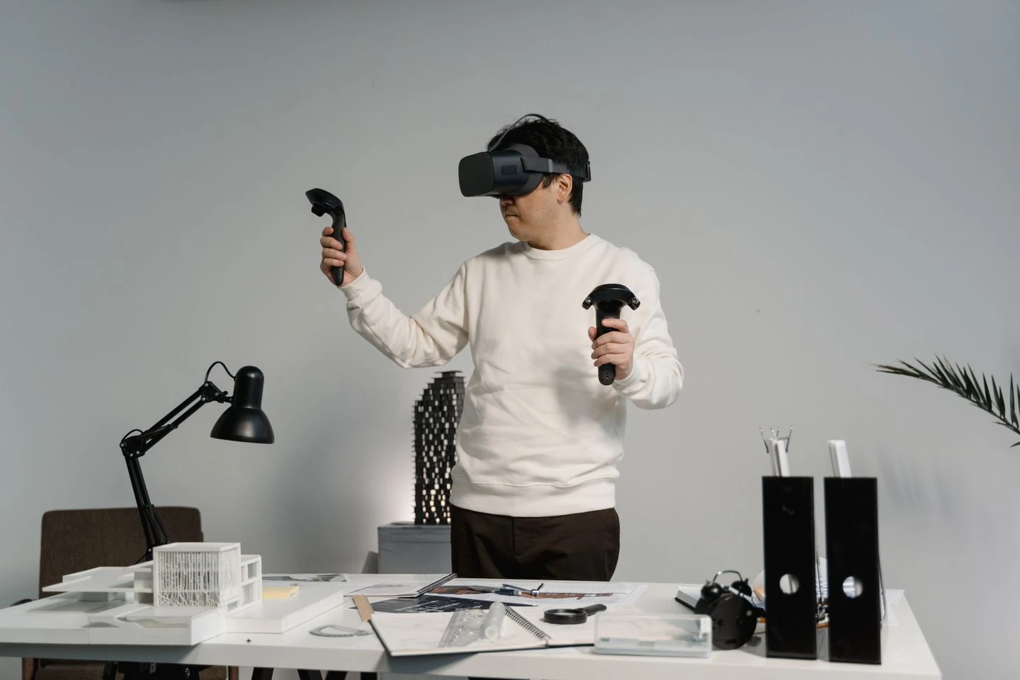 Person wearing a VR headset and holding two motion controllers in a workspace